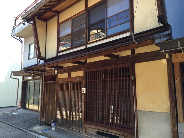 A traditional Japanese building with a wooden structure, large sliding doors, and a small garden area with a potted plant. - Yanaka No Taisuke (Gujo)