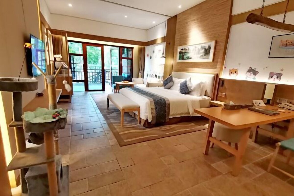 Una habitación de hotel moderna con una cama grande, un escritorio de madera, un rascador para gatos y vistas al exterior.