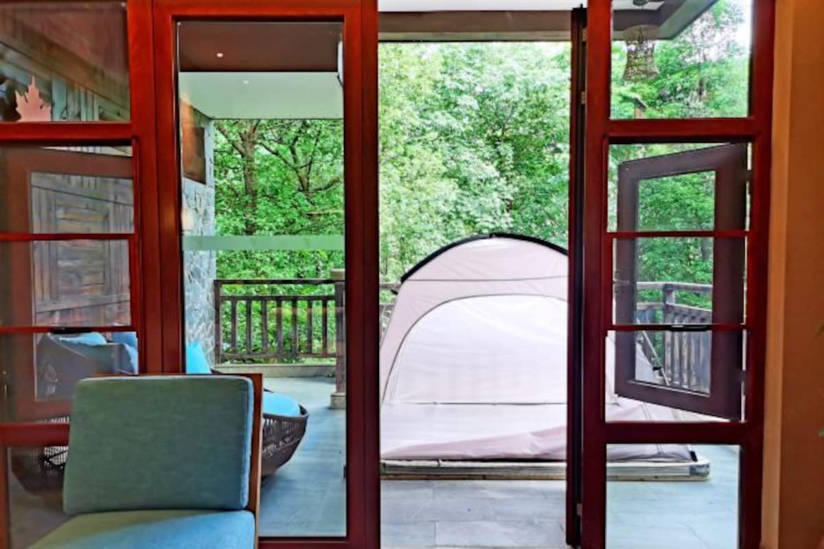 A room with a view of a tent set up outside, a chair, and a table.