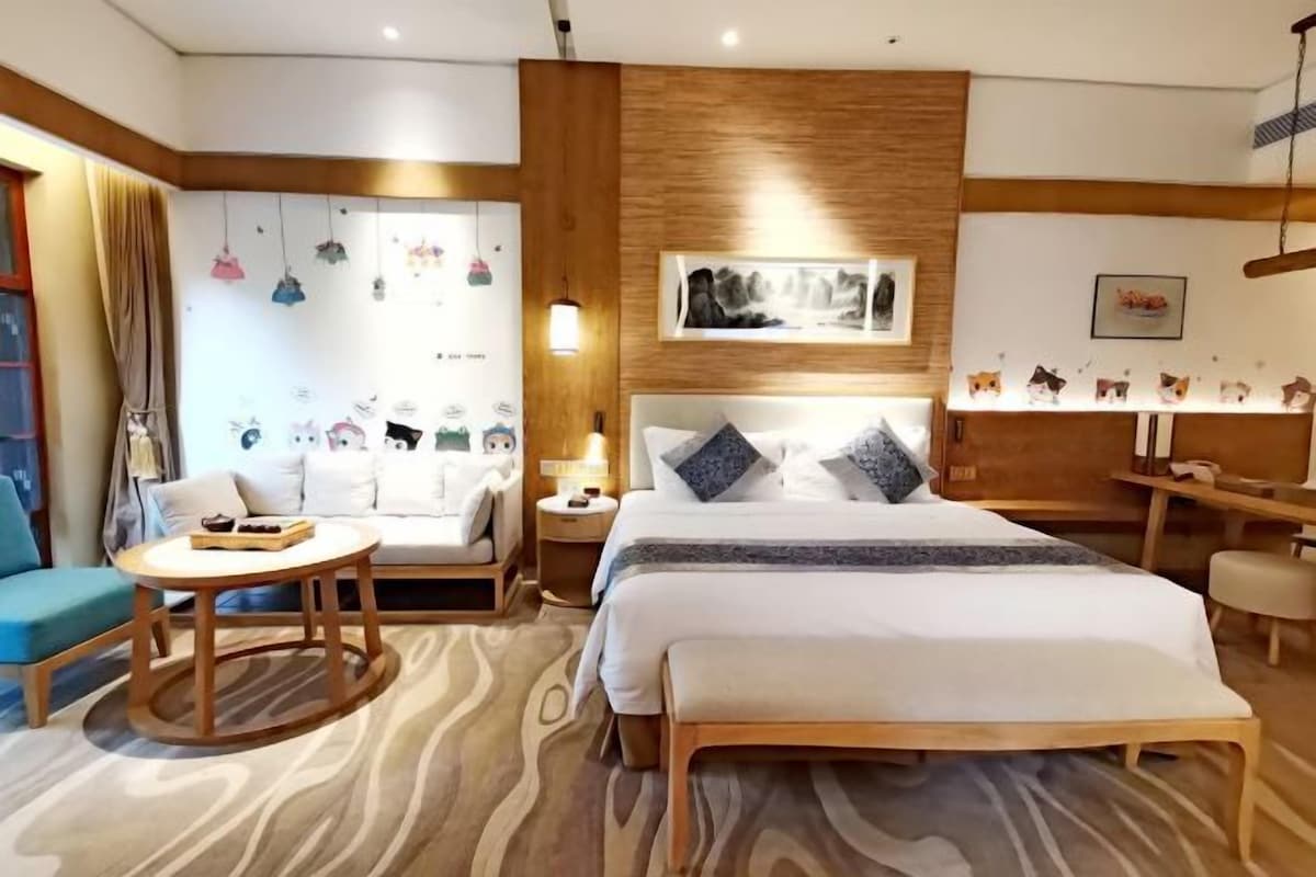 A modern hotel room with a large bed, a round wooden table, a sofa, and a desk.