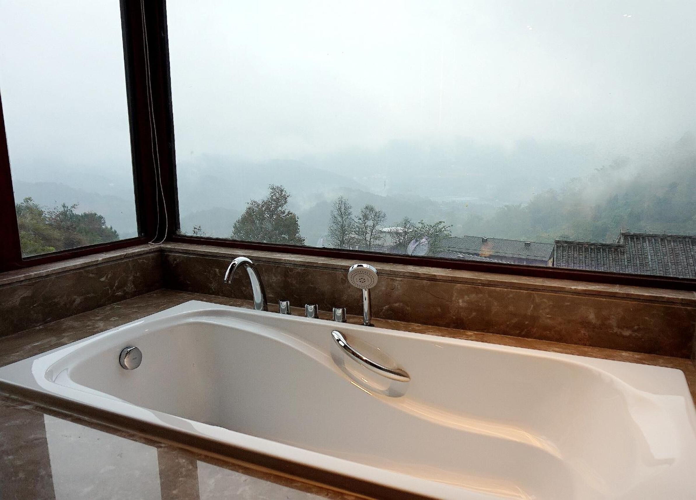 Ein Badezimmer mit einer großzügigen Badewanne, einem Fenster und Blick auf eine Berglandschaft.