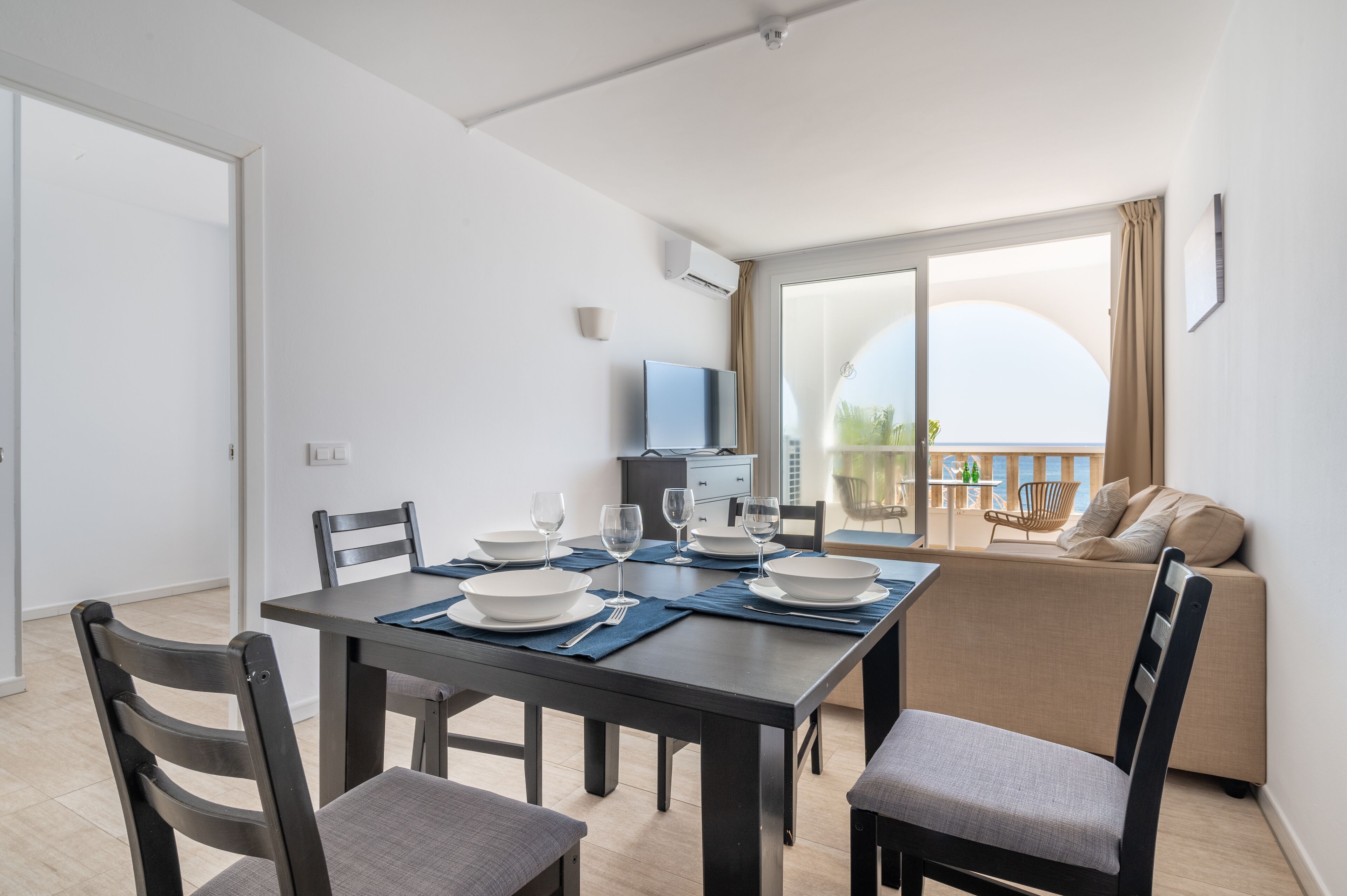 A modern dining area with a table set for four, a sofa, and a balcony with a view.