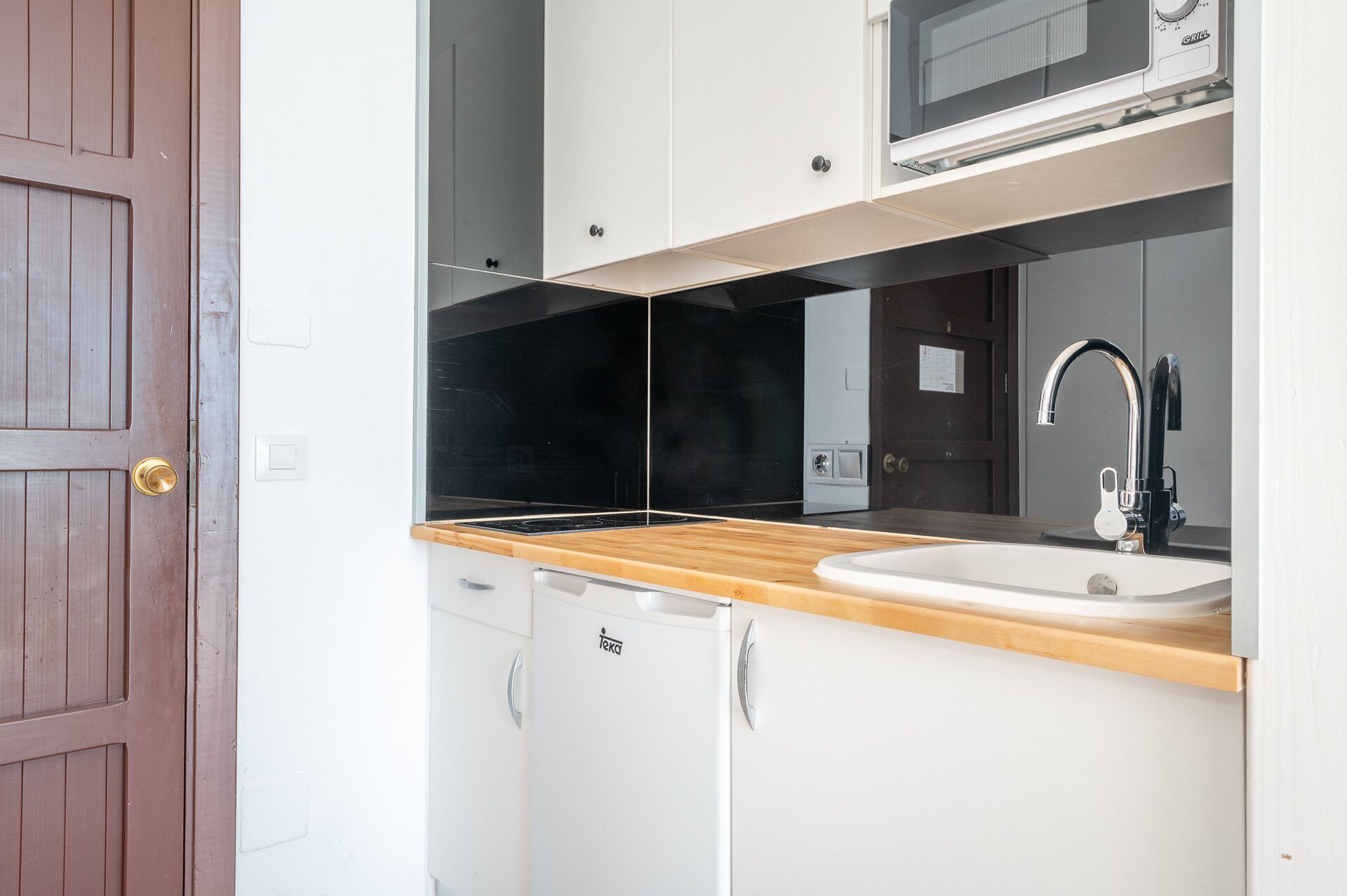 A compact kitchen with a wooden countertop, a white sink, and a built-in microwave.