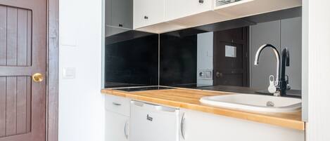 A compact kitchen with a wooden countertop, a white sink, and a built-in microwave.