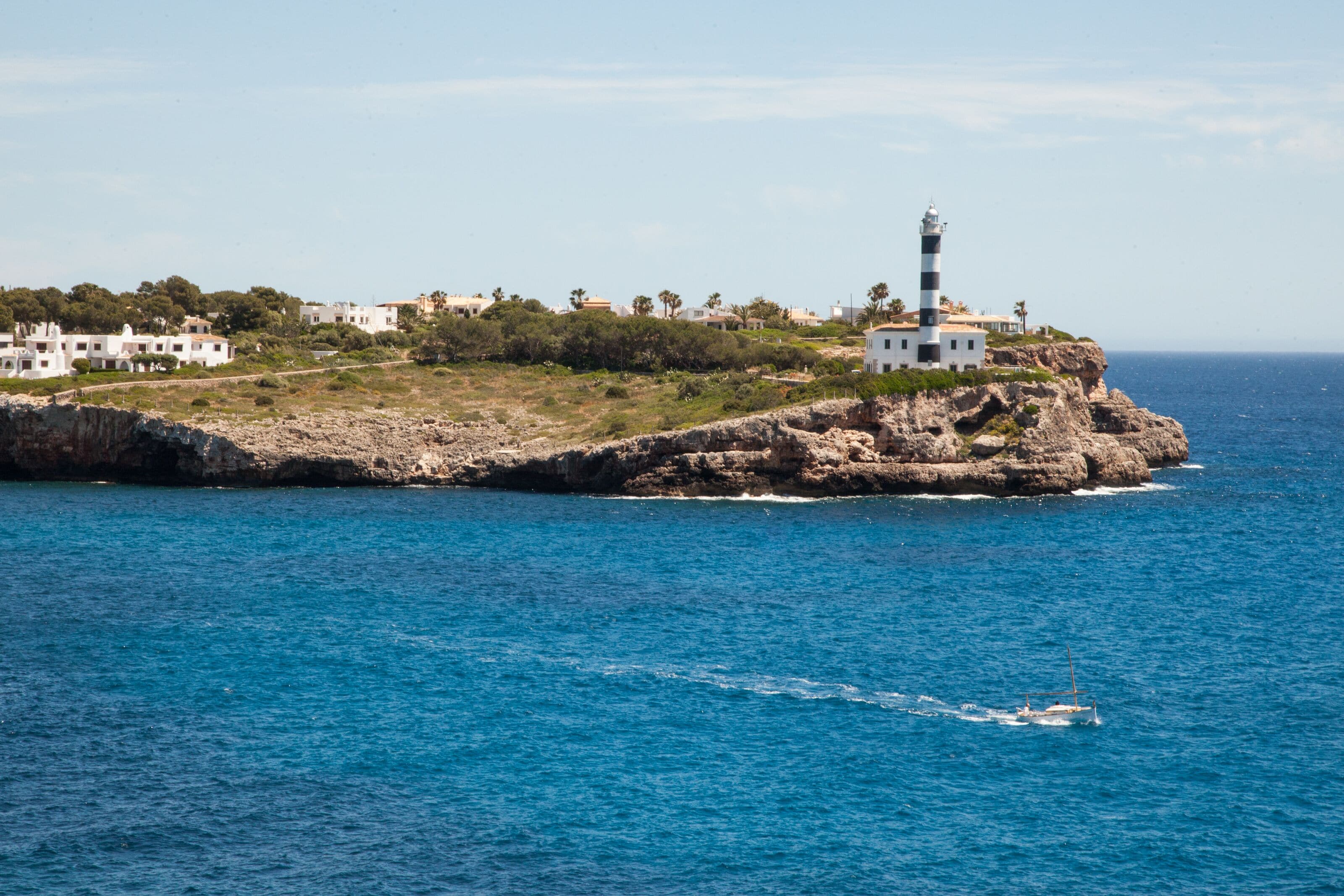 A coastal scene with a lighthouse, rocky terrain, and white buildings.