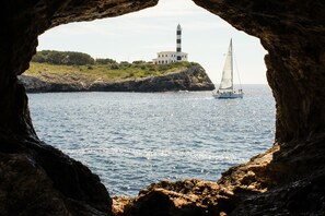 A lighthouse on a rocky island with a sailboat in the water. - Orange Colom Seaside Apartments (Felanitx)