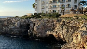 Un hôtel à plusieurs étages, doté de balcons, situé sur une falaise surplombant la mer.