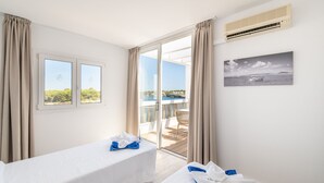 Une chambre d’hôtel avec deux lits, un balcon donnant sur la mer et un tableau accroché au mur.