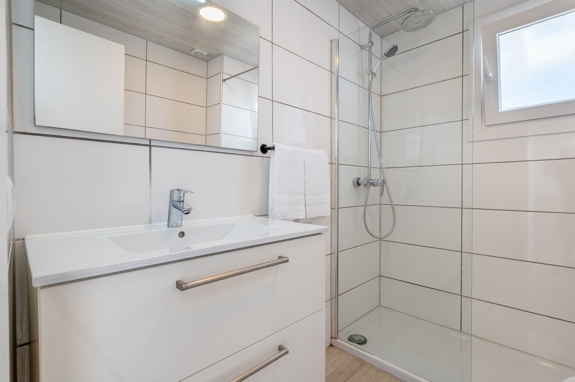 A modern bathroom with a white sink, mirror, and shower.