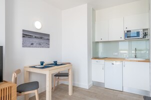 Una cocina moderna con armarios blancos, microondas y lavavajillas. Hay una mesa de comedor con dos sillas y un cuadro de un paisaje nevado en la pared.