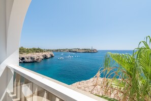 A coastal view from a balcony with a clear blue sea, rocky coastline, and a lighthouse in the distance. - Orange Colom Seaside Apartments (Felanitx)