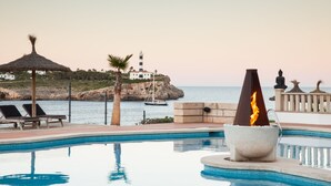 Un espace piscine doté de chaises longues, d’un foyer extérieur, d’une statue et offrant une vue sur la mer et un phare.