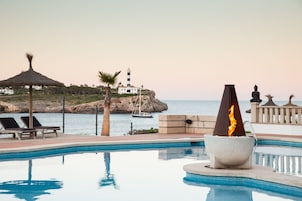 Un área de piscina con sillones de descanso, una chimenea, una estatua y vistas al mar y un faro.