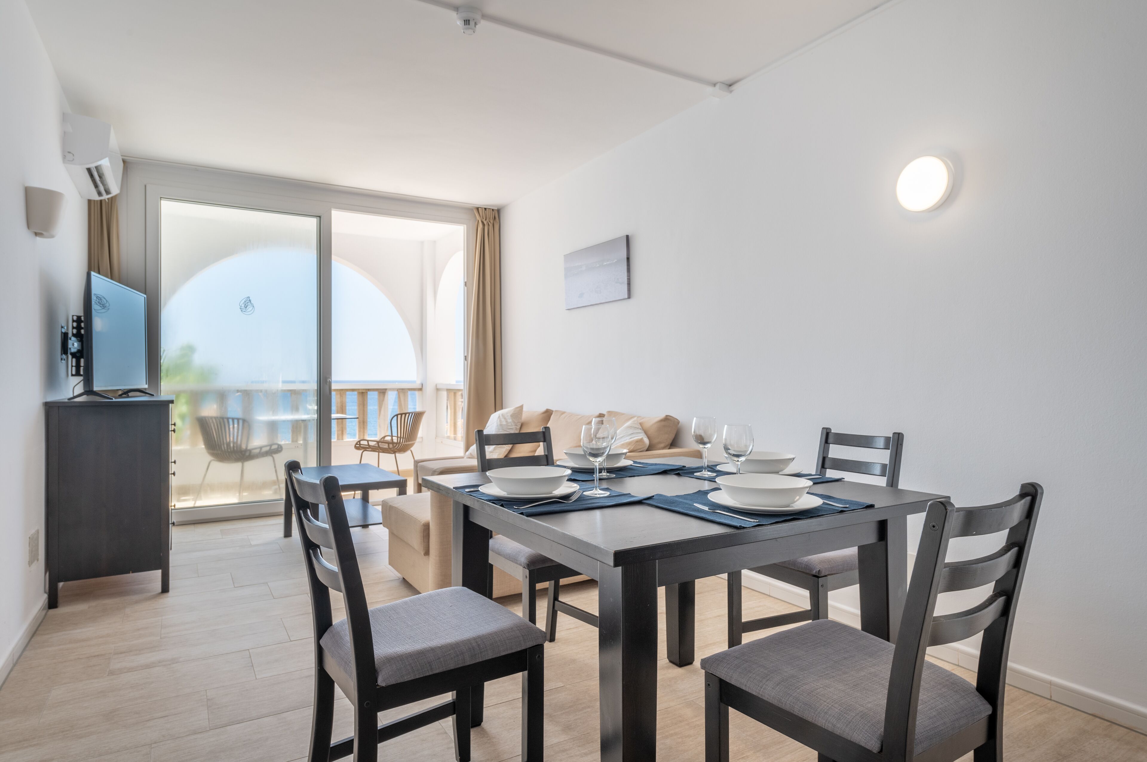 Un comedor con una mesa dispuesta para cuatro, sillas, un sofá y un televisor sobre un mueble.