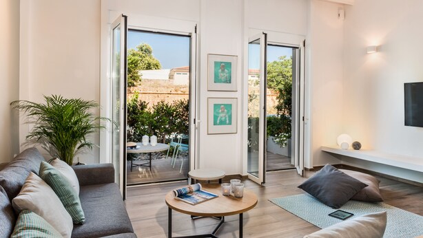 A modern living room with a sofa, a coffee table, and a TV. There are two doors leading to an outdoor area with a table and chairs. - No17 Pireos Street (Chania)