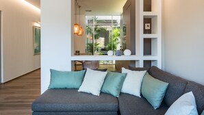 A modern living room with a grey sofa, teal cushions, a large mirror, and a view of a balcony with plants. - No17 Pireos Street (Chania)
