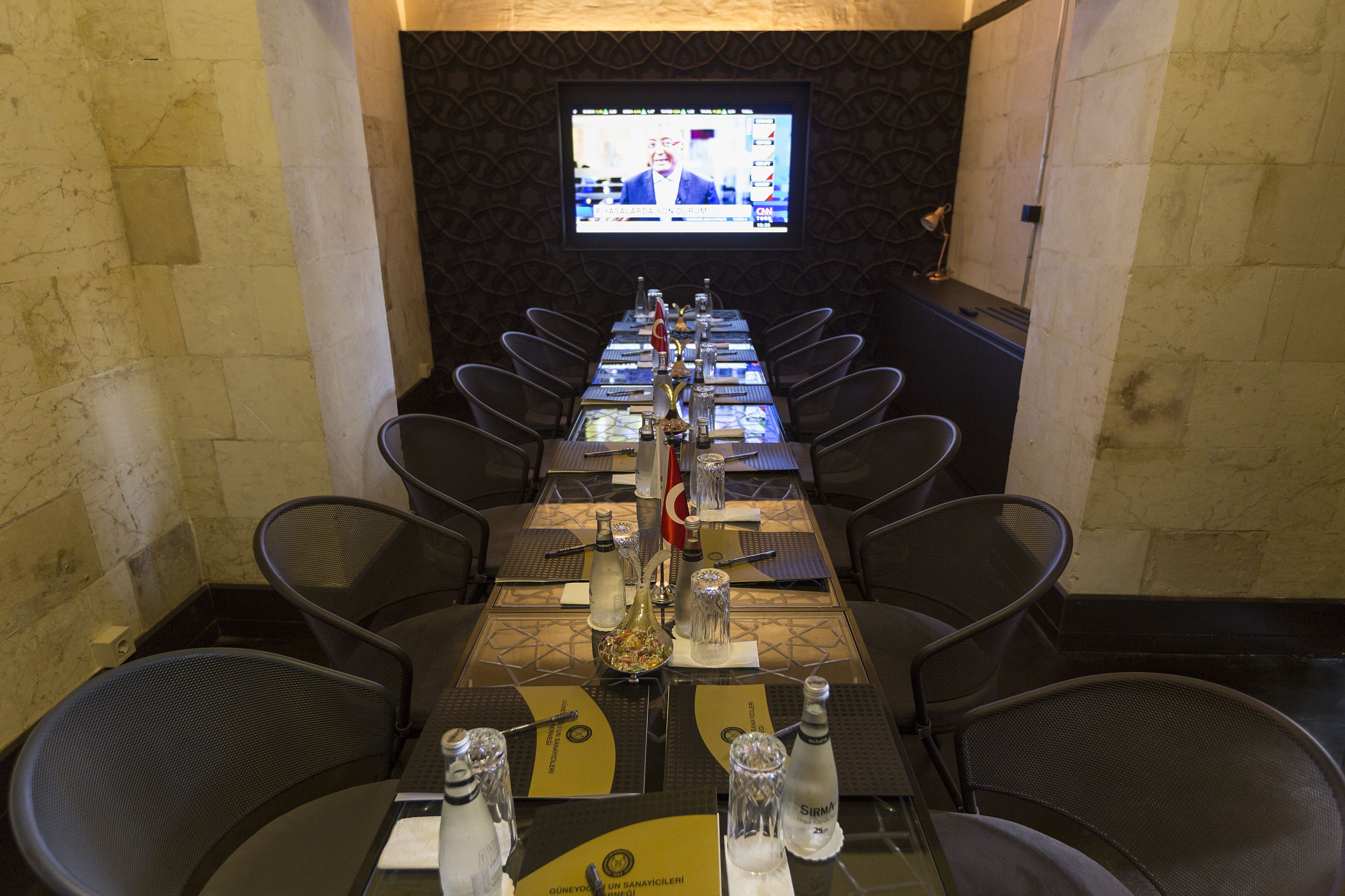 A conference room with a long table, chairs, and a television screen displaying a news broadcast.