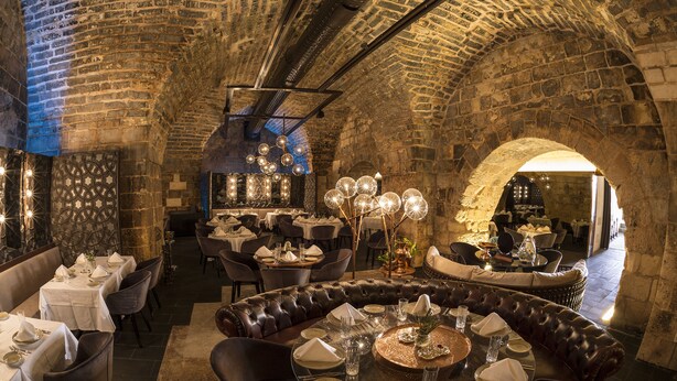 Un restaurant aux murs de pierre, doté de sièges en cuir et de tables dressées pour le service.