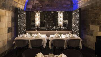Un restaurant doté d’une voûte, de tables rondes dressées pour le dîner et d’un luminaire moderne placé au-dessus des tables.