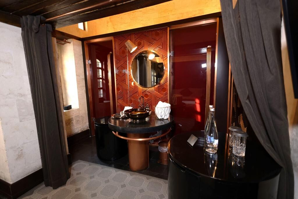 A bathroom with a round mirror, a sink, and a round table with bottles.