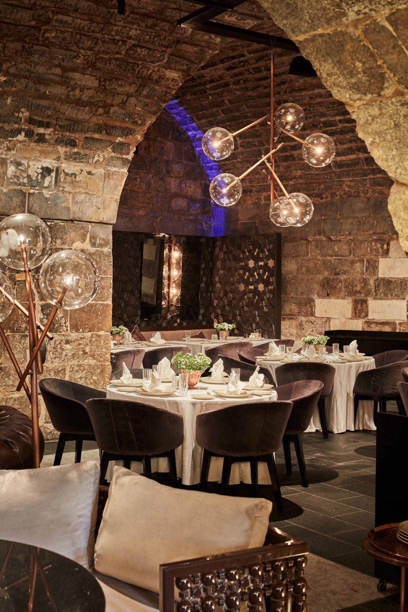 A restaurant with stone walls, round tables, and modern lighting fixtures.