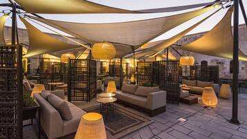 Un espace extérieur aménagé avec des canapés, des tables et un éclairage décoratif, le tout entouré d’un auvent ombragé.