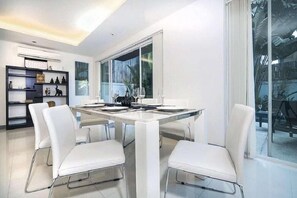 A modern dining area with a glass table, white chairs, and a large window.
