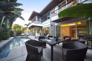 A modern two-story house with a swimming pool, outdoor seating, and large windows.