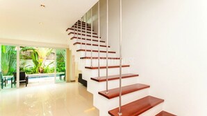 A modern staircase with wooden steps and metal railings, leading to an outdoor area with a pool and greenery. - Villa Cheloni 3 Bedrooms (Kamala)