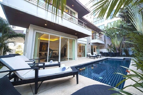 A modern hotel with a swimming pool, lounge chairs, and tropical plants.