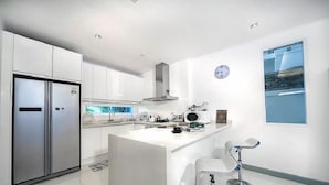 A modern kitchen with white cabinetry, a stainless steel refrigerator, a microwave, and a coffee maker on the counter. - Villa Cheloni 3 Bedrooms (Kamala)