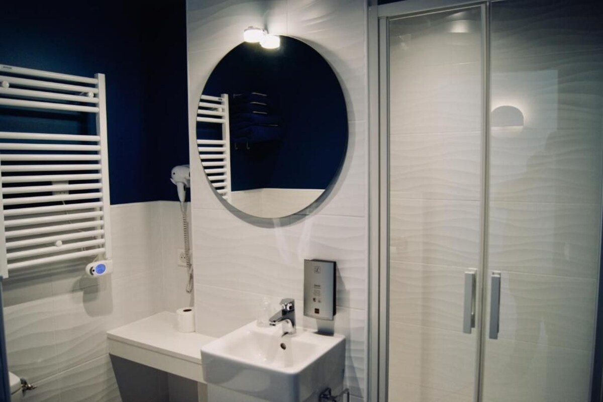 A bathroom with a white sink, a mirror, a towel rack, and a glass shower enclosure.