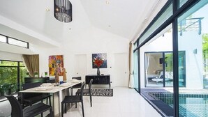 Un espace de salle à manger moderne avec une longue table, des chaises noires et un tapis à motifs noir et blanc. Un tableau orne le mur et un lustre est suspendu au-dessus de la table.