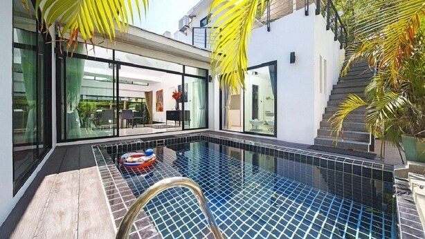 Un espace piscine moderne avec des portes vitrées donnant sur un coin repas, le tout entouré de palmiers.