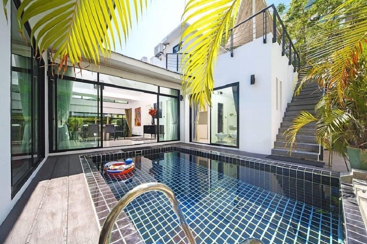 Ein moderner Poolbereich mit Glastüren zu einem Essbereich, umgeben von Palmen.
