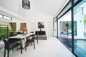 A modern dining area with a glass table, black chairs, and a view of a swimming pool. - Villa Kamala Regent 3-4 Bedrooms (Kamala)