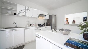 Une cuisine moderne avec des meubles blancs, un réfrigérateur en acier inoxydable et un îlot central doté d’une bouilloire et d’un saladier.