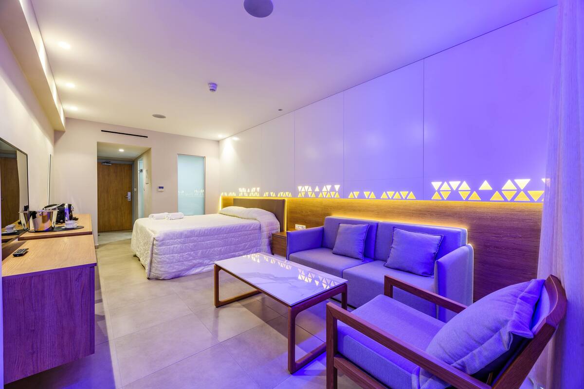 Moderni hotellihuone, jossa on sänky, sohva, työpöytä ja taustalla näkyy kylpyhuone.