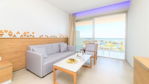 Ein modernes Hotelzimmer mit grauem Sofa, einem Holztisch und einem Balkon mit Blick auf die Stadt.