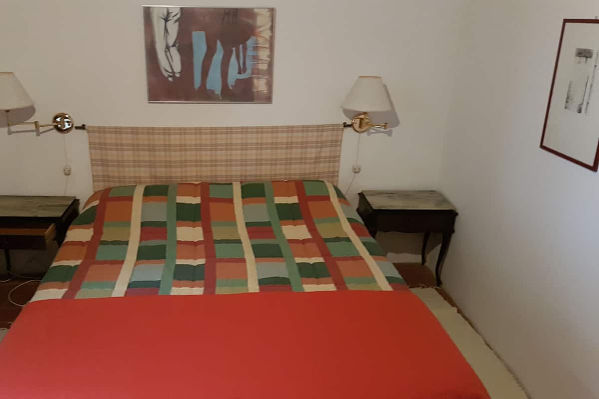 A bedroom with a plaid headboard, a colorful quilt, two bedside tables, and wall-mounted lamps.
