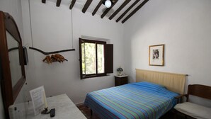 Un dormitorio con cama, una silla, un escritorio, un ventanal y un cuadro en la pared.
