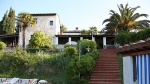 Un edificio con techo de tejas, una escalera que lleva a un área cubierta, y mobiliario exterior con sillas y una mesa.