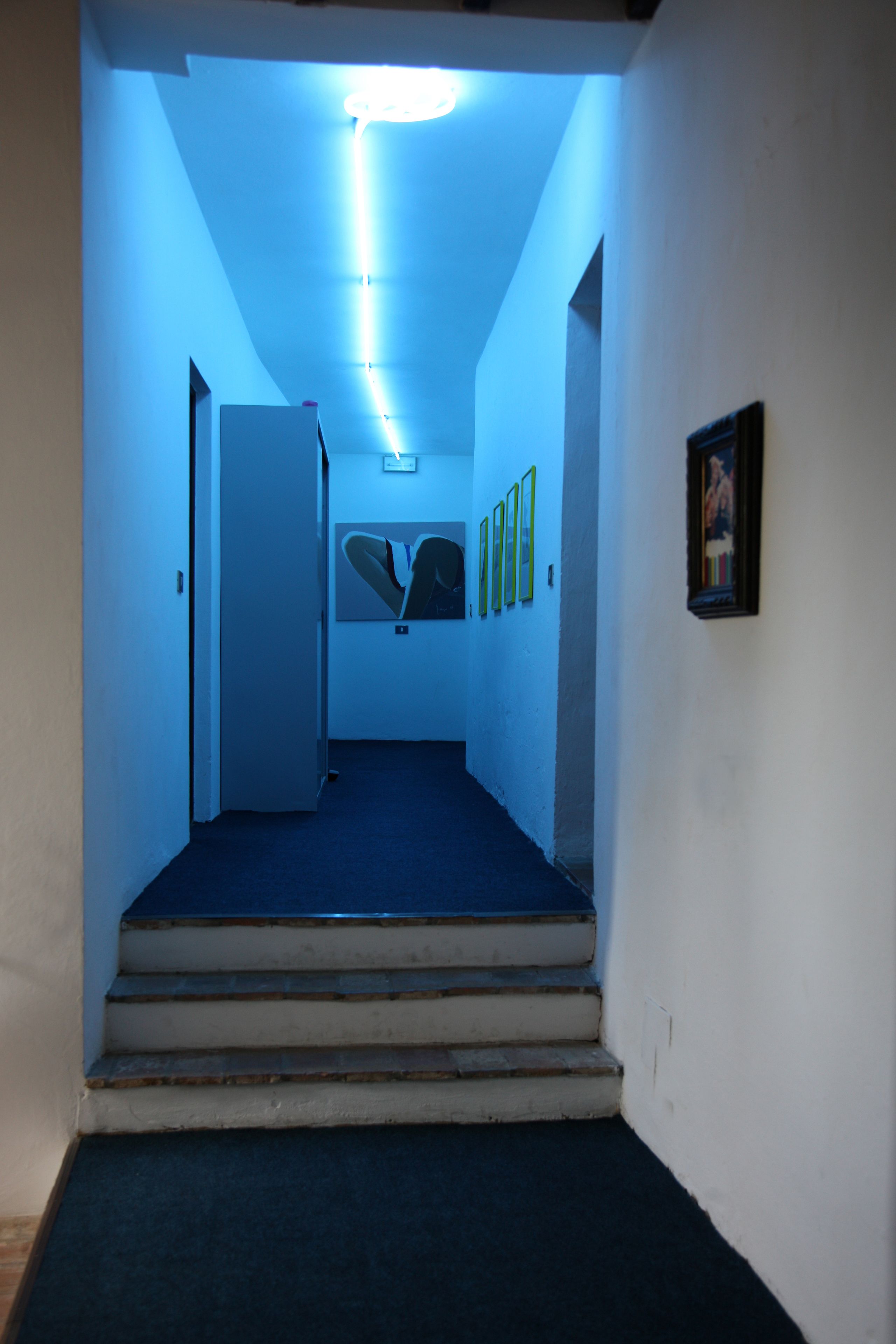 A hallway with a blue carpet, a staircase, and framed pictures on the walls.
