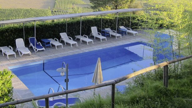 Una piscina con sillones de descanso y una pérgola.