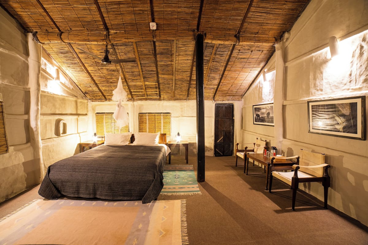 A room with a bed, a desk, and a chair. There are pictures on the wall and a window with blinds.
