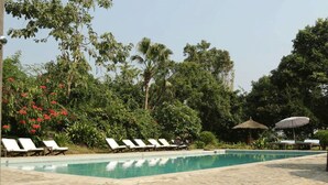 Ein Poolbereich mit Liegestühlen und Sonnenschirmen, umgeben von üppiger Vegetation und Bäumen.