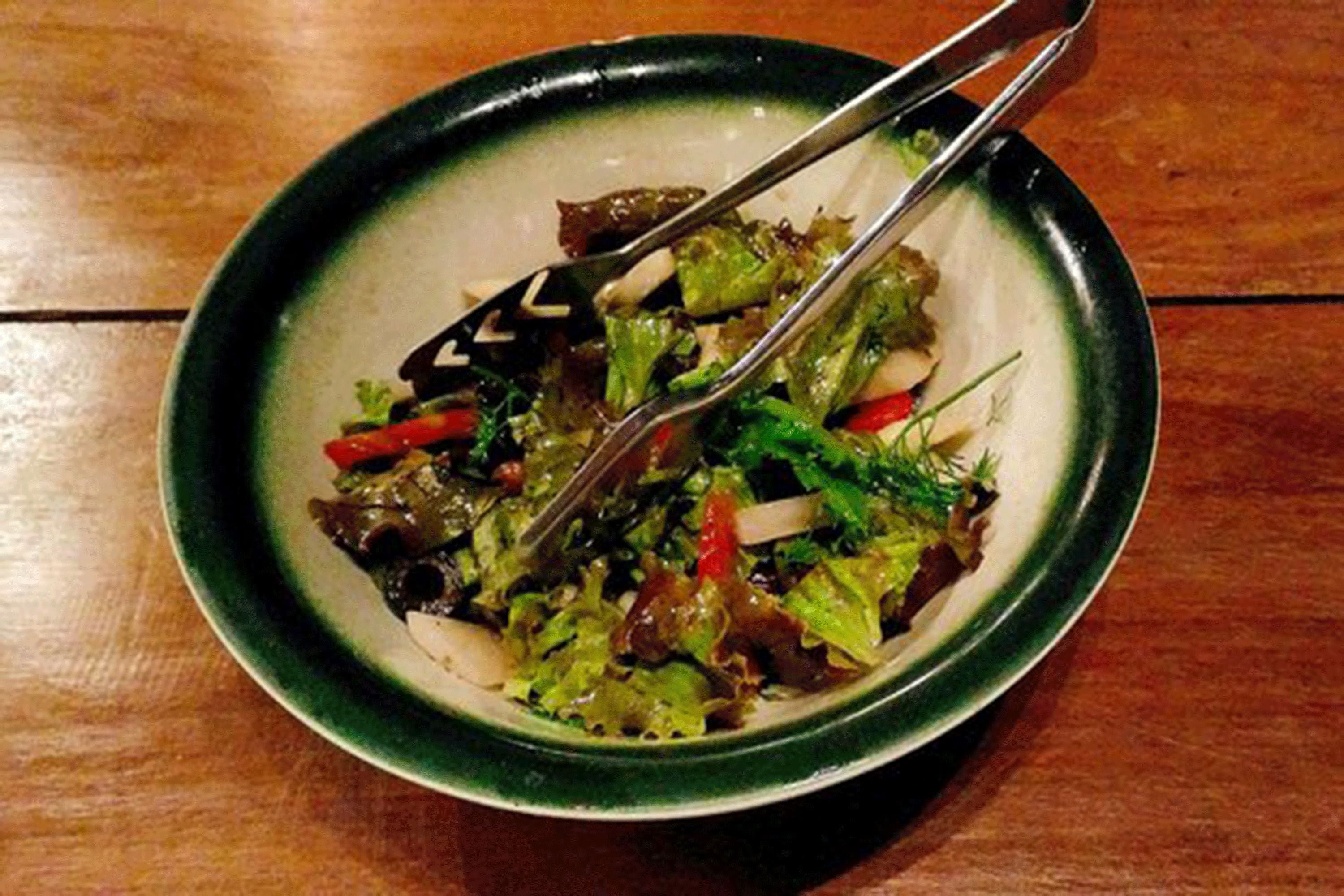 A bowl of salad with mixed greens and vegetables on a wooden table.