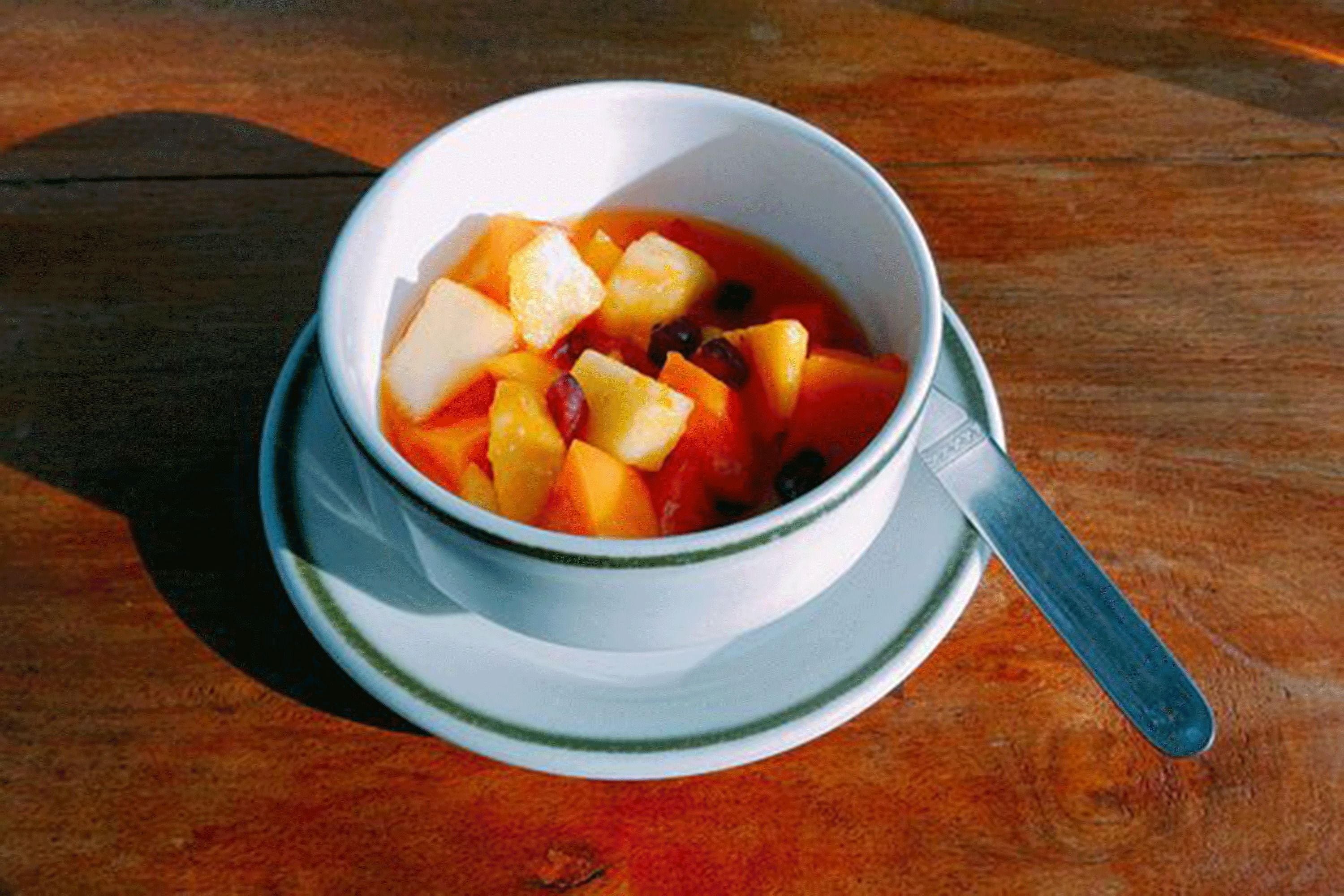 A bowl of fruit soup on a white plate with a spoon.