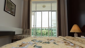 Een hotelkamer met een bed, een stoel, een bureau, een lamp en een groot raam met gordijnen.