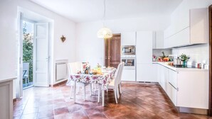 A modern kitchen with white cabinets, a dining table set for four, and a large window. - Maison Palazzo Correale (Sorrento)